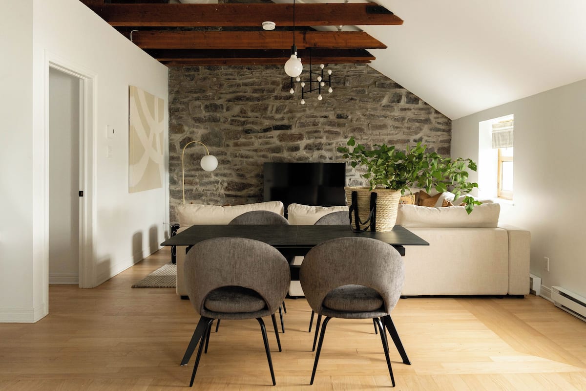 A dining area with a stone wall, a black table, and two grey chairs.
