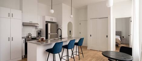 Una cocina moderna con armarios blancos, una isla central con taburetes de bar, una mesa de comedor e iluminación colgante.