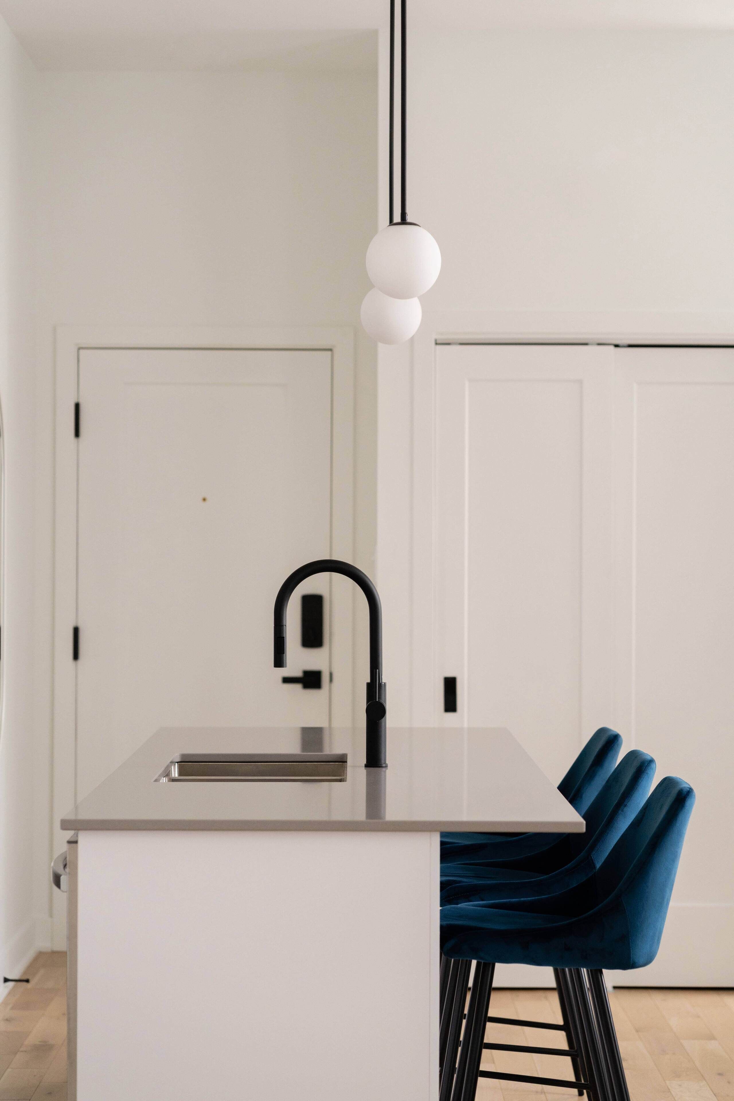 Eine moderne Küche mit einer weißen Arbeitsplatte, einem schwarzen Wasserhahn und blauen Barhocker.