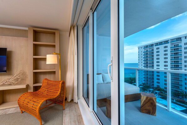 A modern hotel room with a large sliding glass door leading to a balcony with a city view.