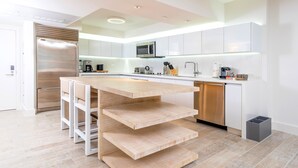 Une cuisine moderne dotée d’un îlot central, d’appareils électroménagers en acier inoxydable et de meubles de rangement blancs.