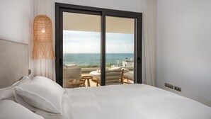 Habitación de hotel con una cama grande, vistas al océano y un balcón con mobiliario exterior.