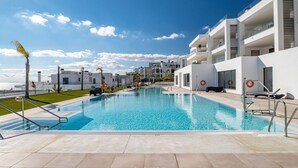 Un hotel moderno con piscina, balcones blancos y cielo despejado.