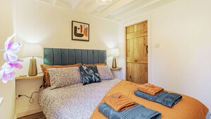 Une chambre à coucher comprenant un lit, deux tables de chevet, une porte en bois et une œuvre d’art accrochée au mur.