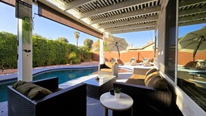 A covered outdoor area with a pool, wicker furniture, and a table with a potted plant. - SantaFe Desert Oasis: Saltwater Pool, EV Charger, Near Coachella & Tennis Garden (Indio)