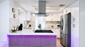 A modern kitchen with white cabinetry, stainless steel appliances, and a central island with a purple-lit base. - SantaFe Desert Oasis: Saltwater Pool, EV Charger, Near Coachella & Tennis Garden (Indio)