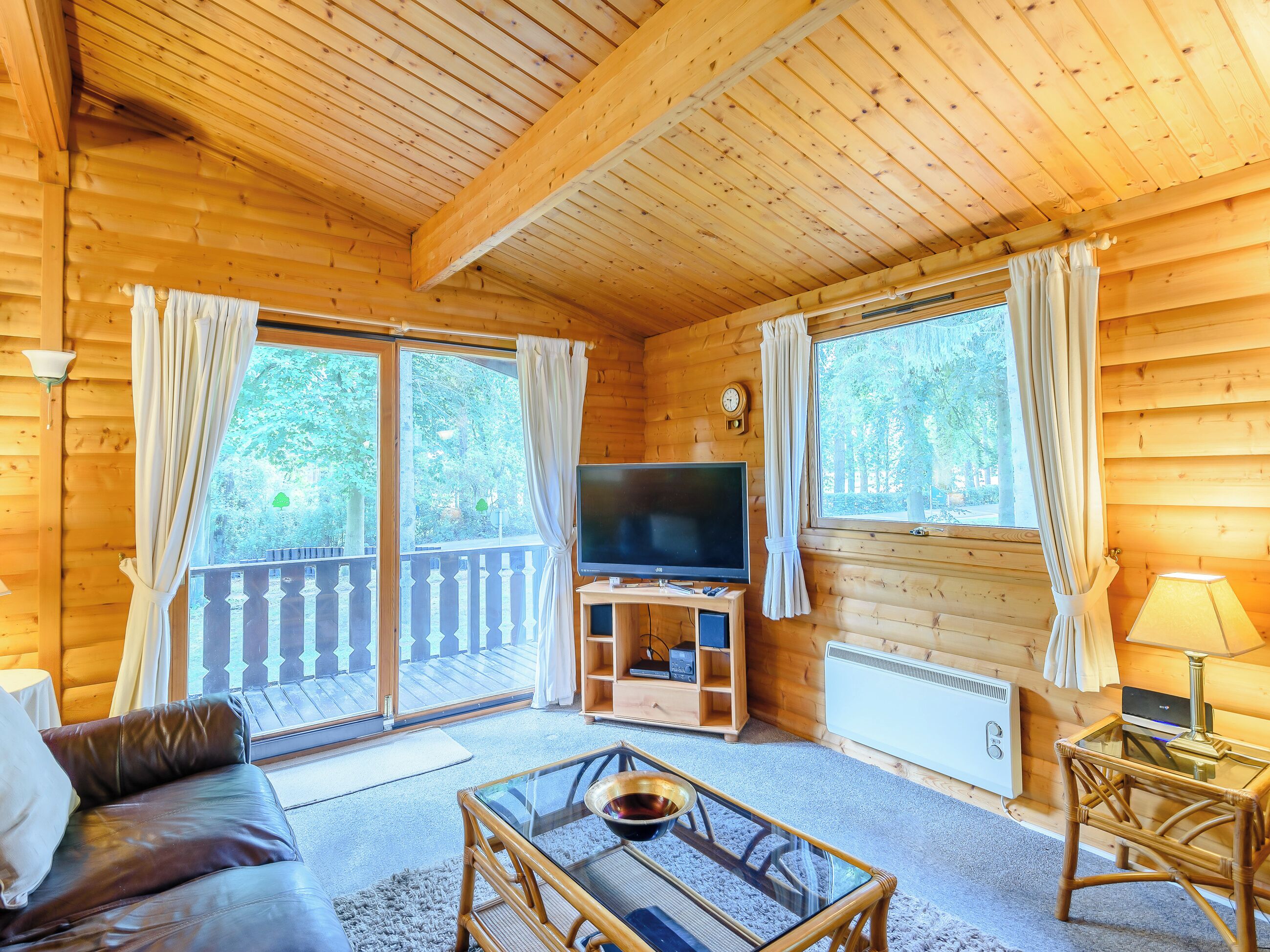 Een houten hut binnen met een bank, een glazen salontafel, een televisie en een balkon met een hekwerk.