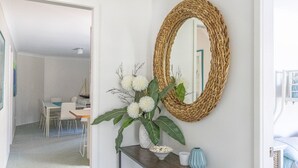 Ein Raum mit einem gewebten Spiegel, einer Vase mit weißen Blumen und einer kleinen blauen Vase auf einer Konsole.