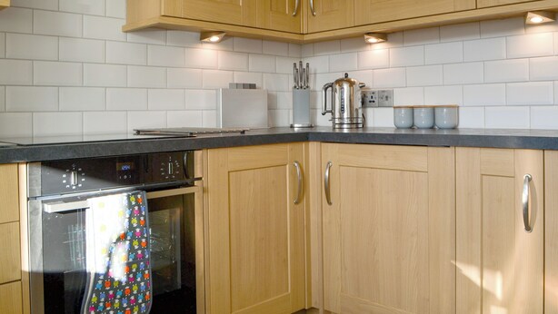 A kitchen with wooden cabinets, a stainless steel appliance, and a tiled backsplash.