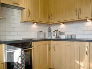 A kitchen with wooden cabinets, a stainless steel appliance, and a tiled backsplash. - 2 bedroom accommodation in Keswick (Keswick)