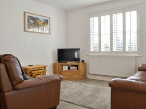 A living room with a television, wooden cabinet, and two leather sofas. - 2 bedroom accommodation in Keswick (Keswick)