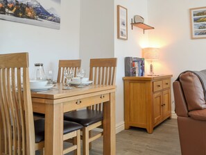 A dining area with a wooden table set for four, a cabinet with books, and a wall-mounted lamp. - 2 bedroom accommodation in Keswick (Keswick)