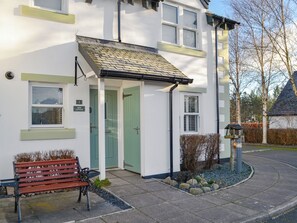 A white building with a green door, a bench outside, and a small garden area with rocks and plants. - 2 bedroom accommodation in Keswick (Keswick)