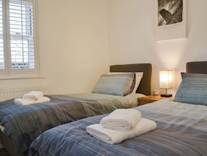 Ein Hotelzimmer mit zwei Betten, einem Fenster mit Jalousien, einem Wandbild und einem Nachttisch mit Lampe.