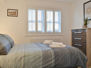 A bedroom with a bed, a dresser, a radiator, and a window with blinds. - 2 bedroom accommodation in Keswick (Keswick)