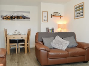 En stue med en brun lædersofa, et spisebord med stole, et maleri på væggen og en lampe.