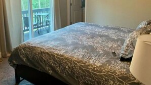 Une chambre avec un grand lit, un balcon avec des chaises et une porte donnant sur une autre pièce.