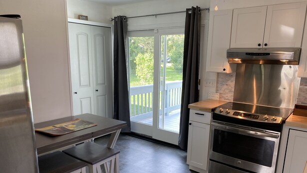 A modern kitchen with a stainless steel refrigerator, a built-in oven, and a gas stove. There is a small dining area with a table and two stools.