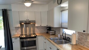 A modern kitchen with white cabinets, stainless steel appliances, a built-in oven, a dishwasher, and a window with blinds.