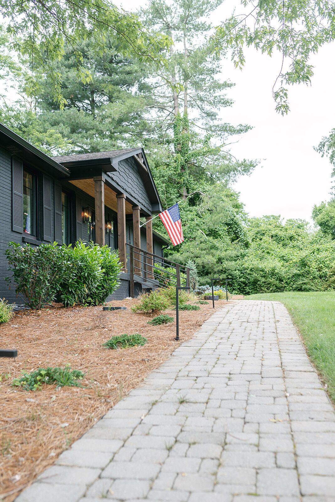 A building with a dark exterior, a porch with railings, and an American flag.