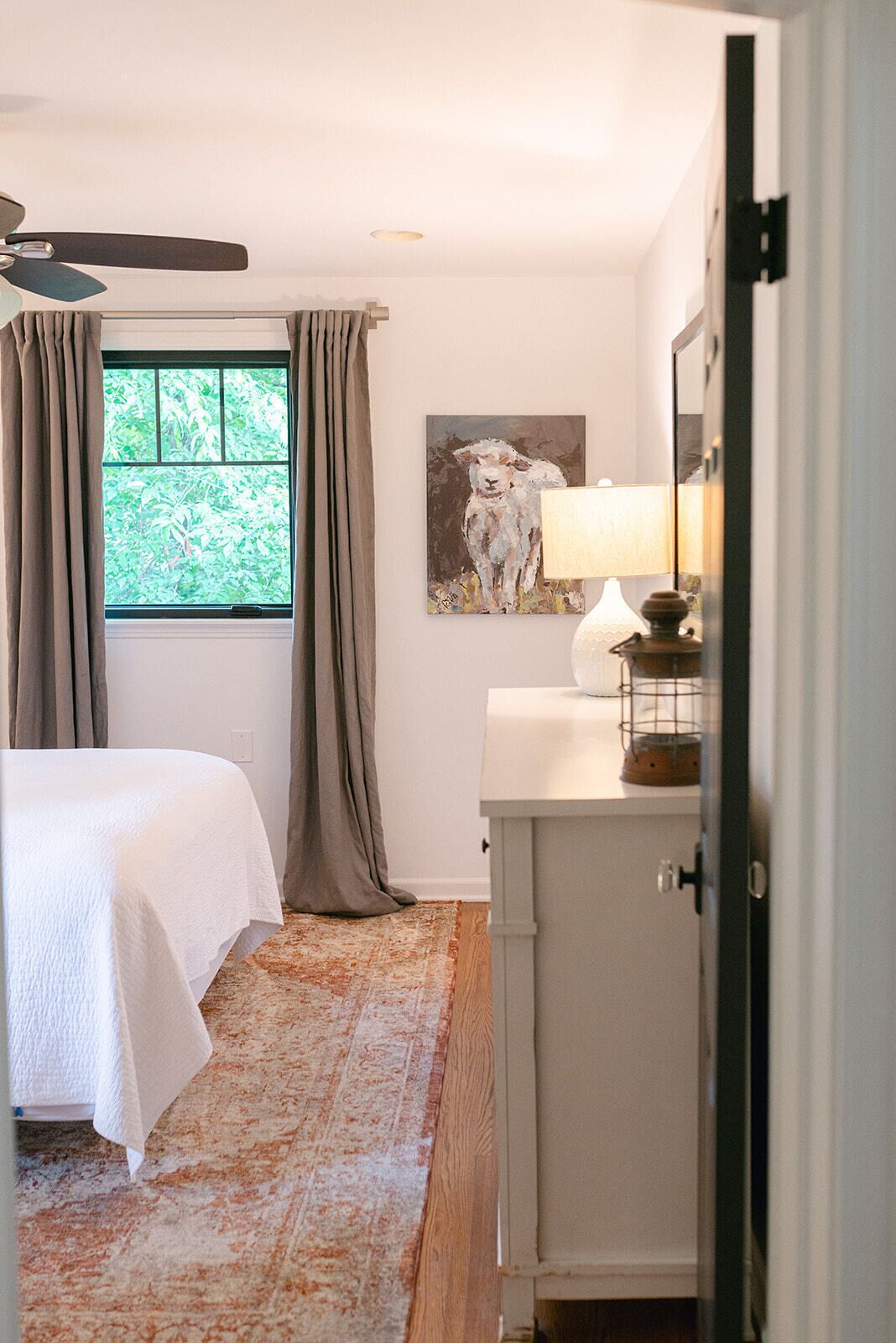 Quarto com cama, janela com cortinas, um quadro, luminária e um armário.