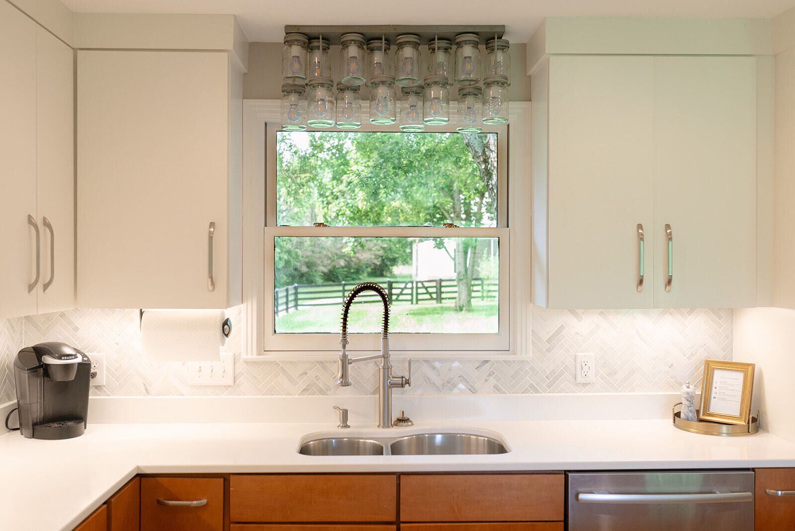 A kitchen with a double sink, a coffee maker, and a window with a view of a green landscape.