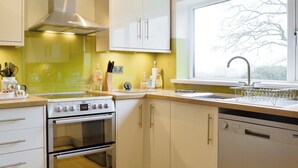 Een keuken met een fornuis, oven, vaatwasser en een raam met uitzicht op bomen.