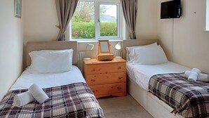Een tweepersoonskamer met twee bedden, een houten nachtkastje, een spiegel en een televisie aan de muur.