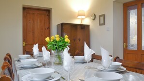 Een eettafel gedekt met witte borden, kommen en bestek, een vaas met gele rozen en een tafelkleed met stippen.
