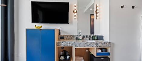 A modern bathroom with a large mirror, vanity, and a flat-screen TV.