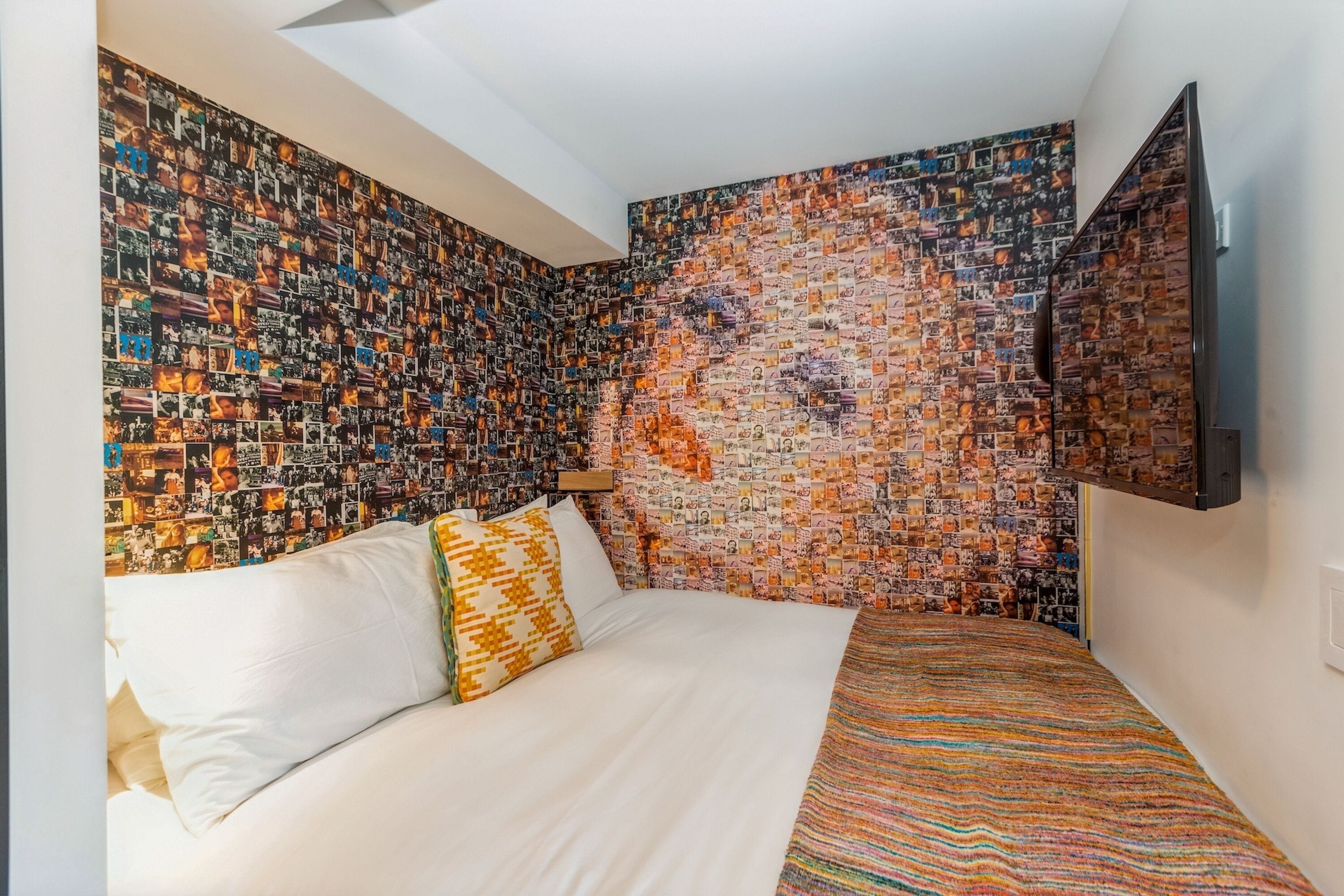 A bedroom with a large bed, a patterned wall, and a flat-screen TV mounted on the wall.