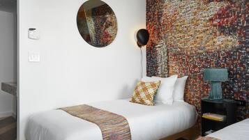 Una habitación de hotel con una cama, un espejo redondo, una pared decorada con fotos, una lámpara y una estantería.