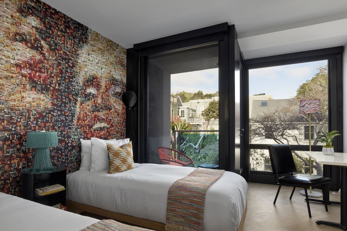 A modern bedroom with a large bed, a small table, a chair, and a balcony with a view of the city.