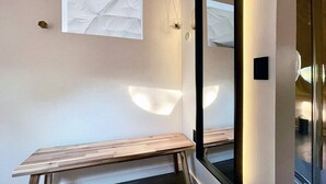 Een minimalistische kamer met een houten bankje, een grote spiegel en een raam met een witte gordijn.