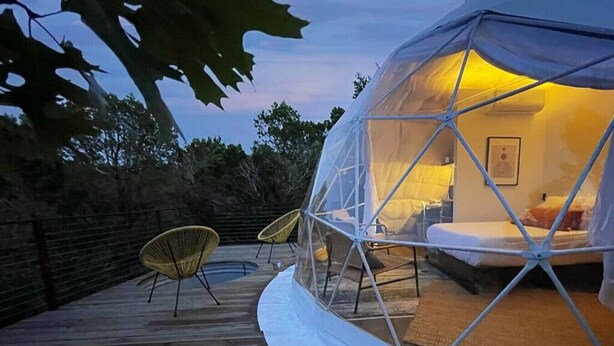 Een koepelvormige tent met een bed van binnen, een klein zwembad en twee stoelen buiten.