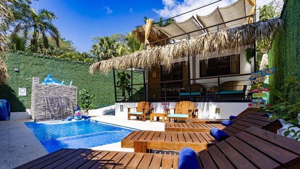 Un área de piscina con tumbonas de madera y una estructura de techo de paja.