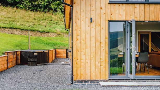 Una cabaña de madera con un área de patio, un jacuzzi y un comedor con mesa y sillas.