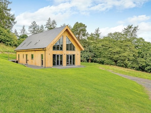 A wooden cabin with a sloped roof, large windows, and a grassy landscape.