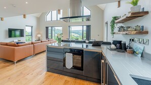 Una cocina moderna con una isla central, un área de comedor con sofá y amplios ventanales con vistas al exterior.