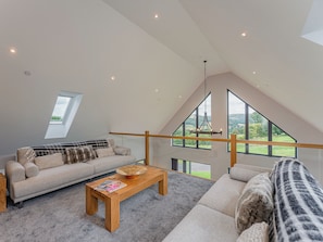 A spacious loft bedroom with a large skylight, a wooden ceiling, and a view of the countryside.