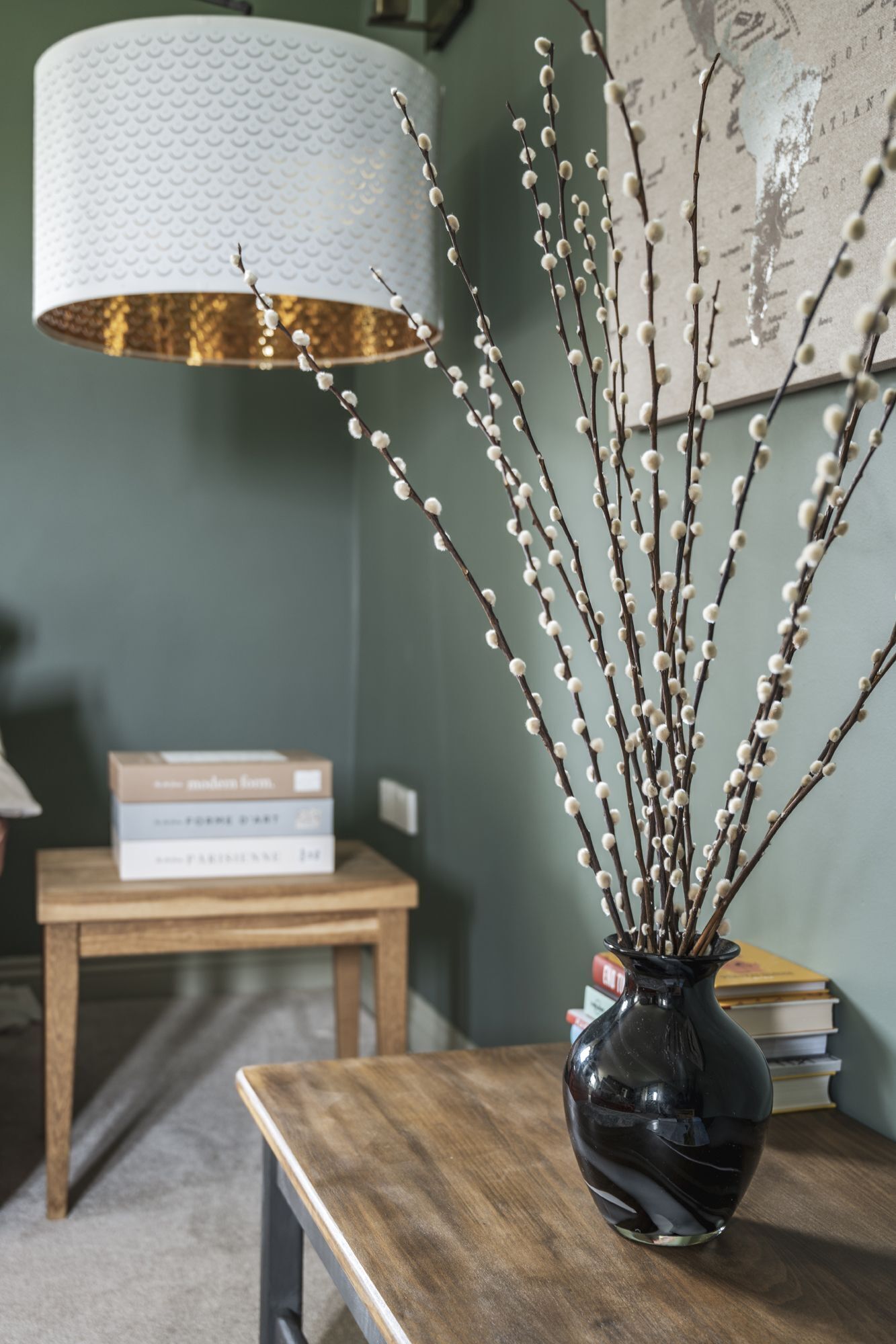 A wooden table with a black vase containing branches with small white flowers.