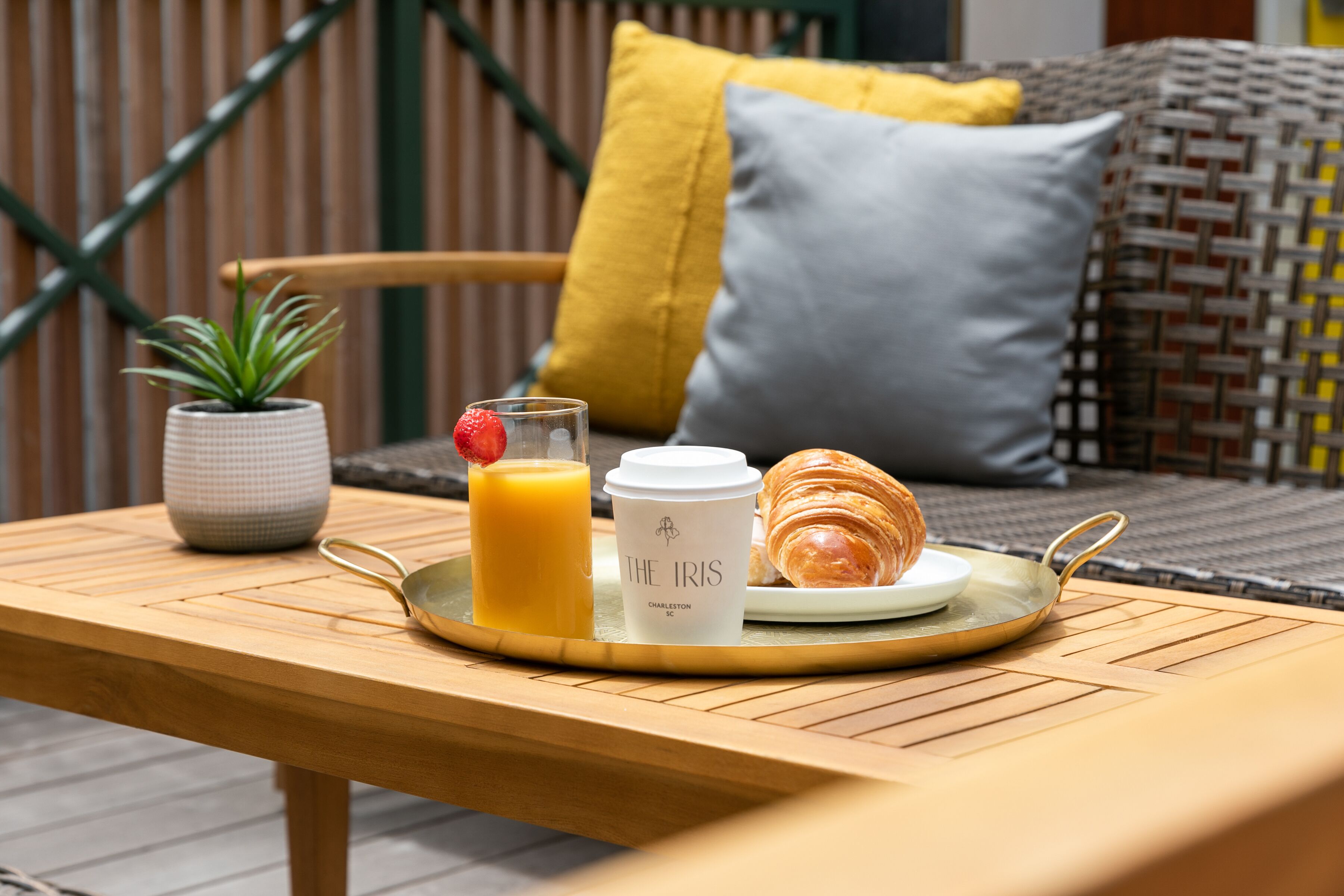 A breakfast tray with a croissant, a glass of orange juice, and a coffee cup on a wooden table.