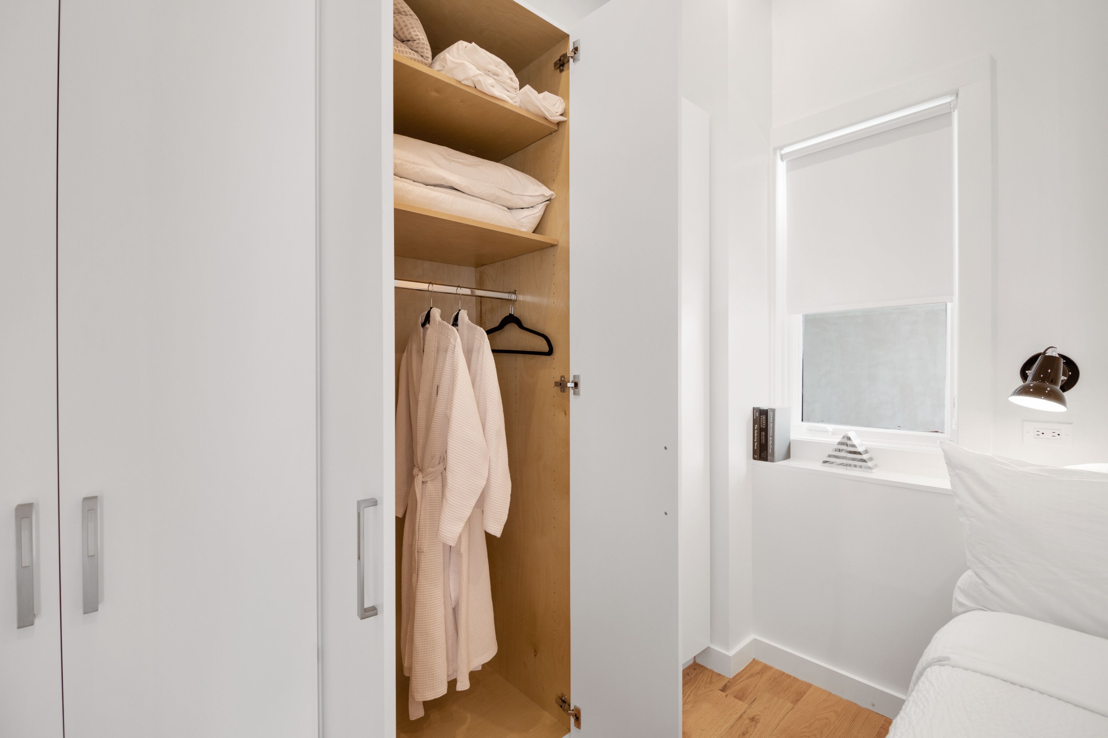 Une pièce blanche avec une armoire en bois, une fenêtre donnant sur un beau paysage et une table de chevet avec une lampe.