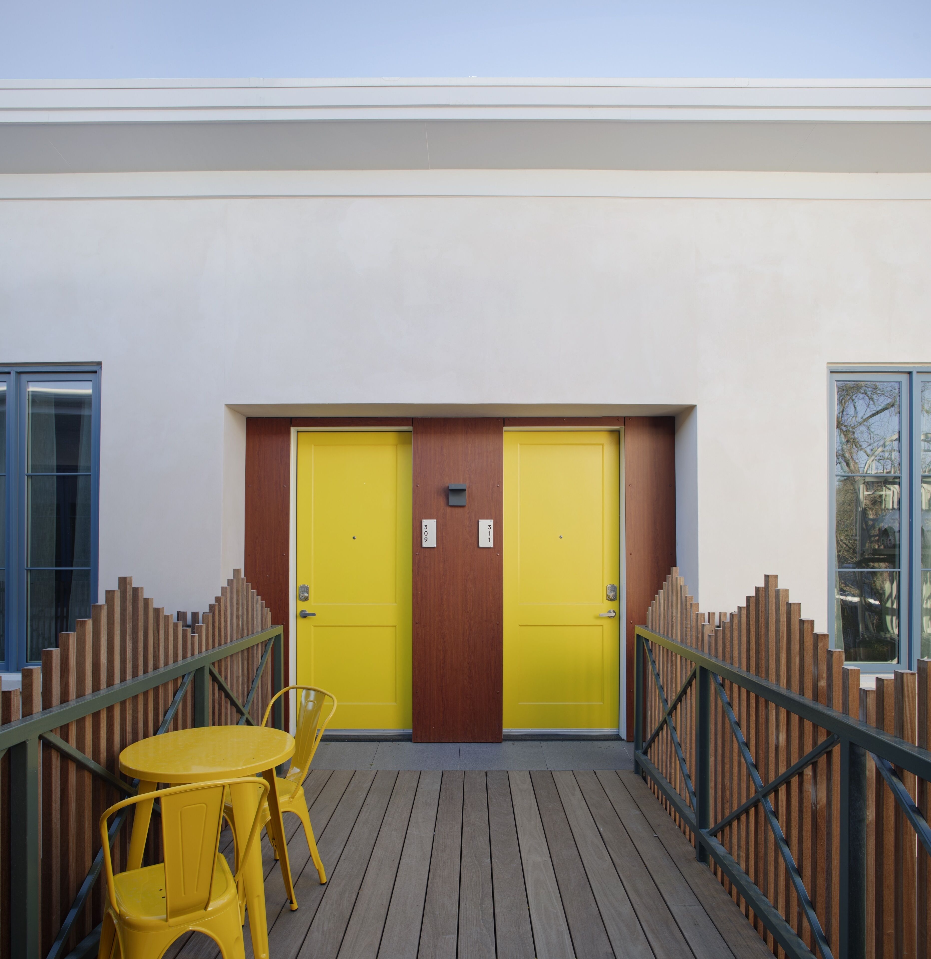 A building with two yellow doors, a wooden deck, and a yellow table with chairs.