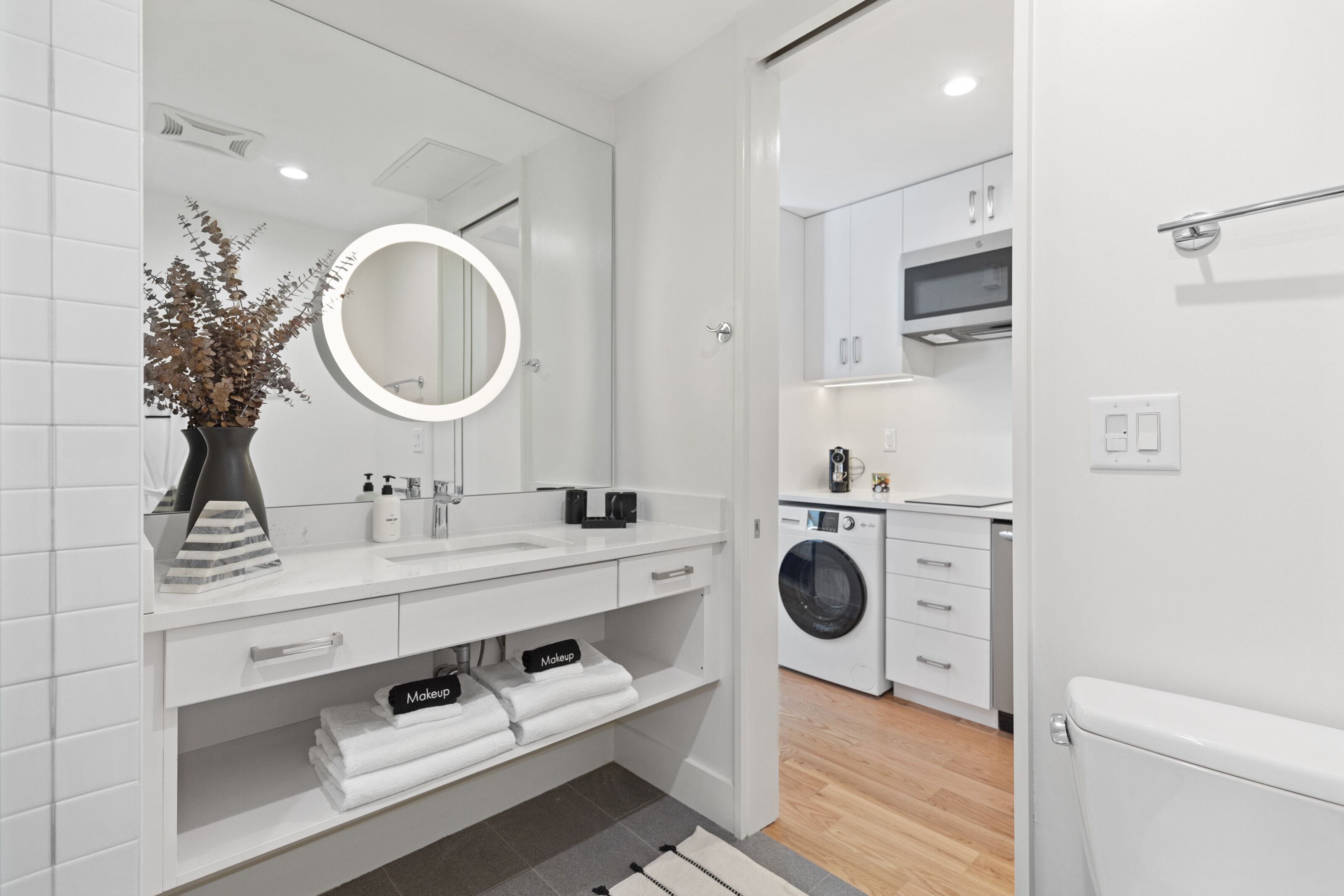 Un baño moderno con un espejo grande, azulejos blancos, un lavabo y un mueble de tocador.