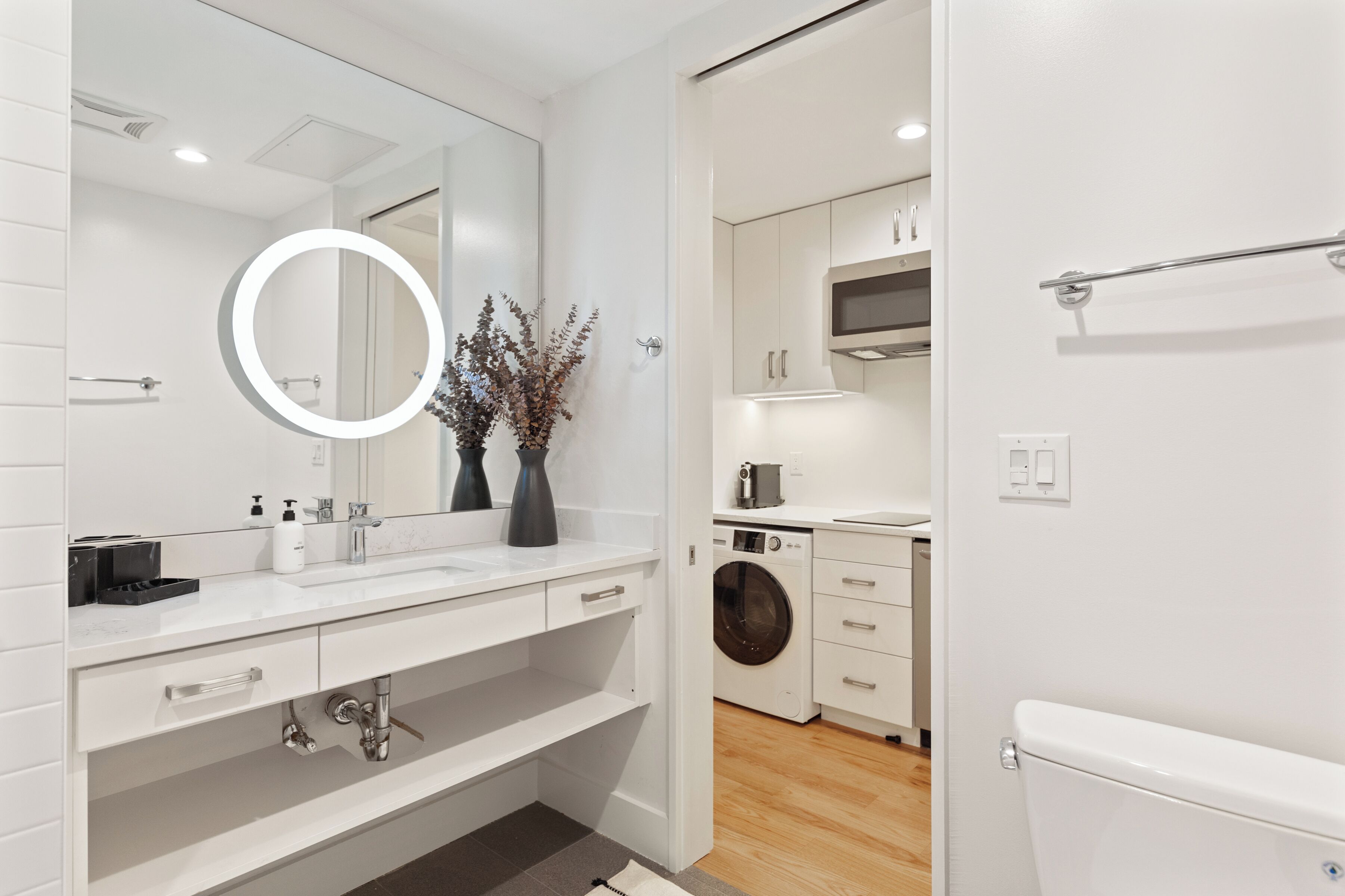 A modern bathroom with a large mirror, white tiles, a sink, and a toilet.