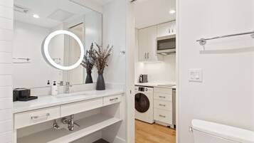 A modern bathroom with a large mirror, white tiles, a sink, and a toilet.