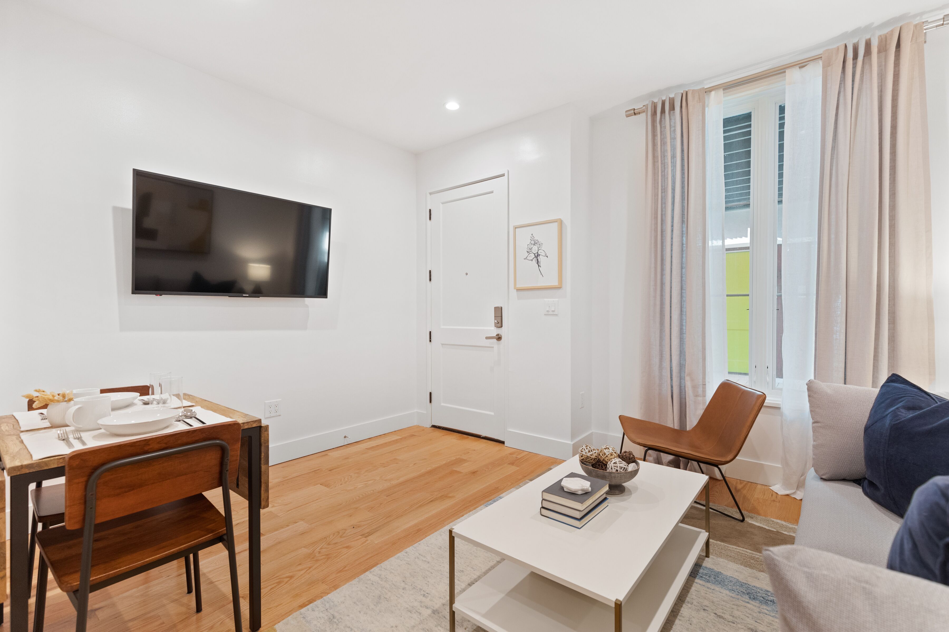 Un salon moderne comprenant un coin repas, un téléviseur à écran plat fixé au mur, un canapé avec des coussins et une table à manger en bois avec des chaises.
