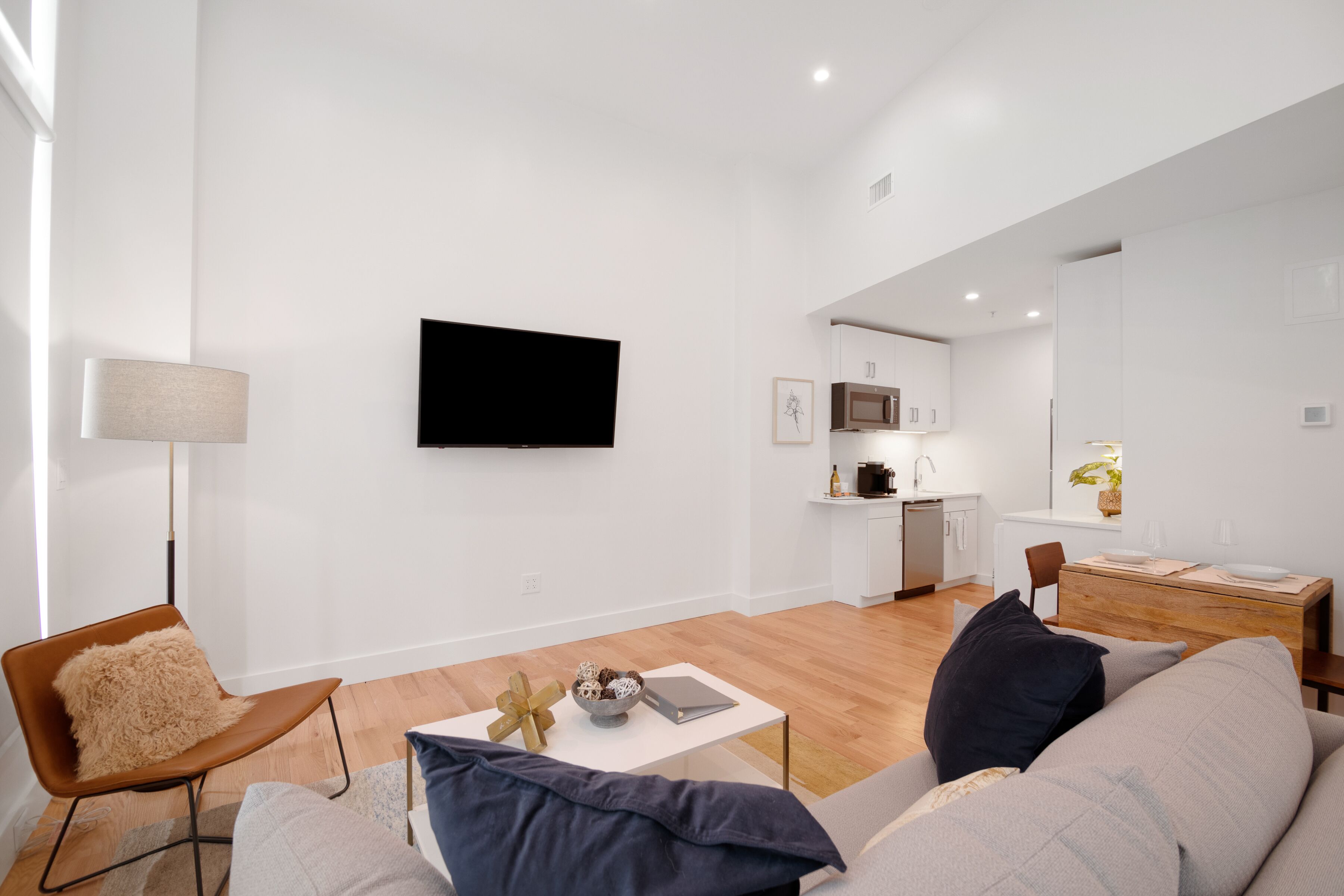A modern living room with a sofa, a coffee table, and a TV. There is a kitchen area in the background.