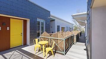 A modern building with a yellow door, a covered outdoor seating area with yellow chairs, and a wooden fence.